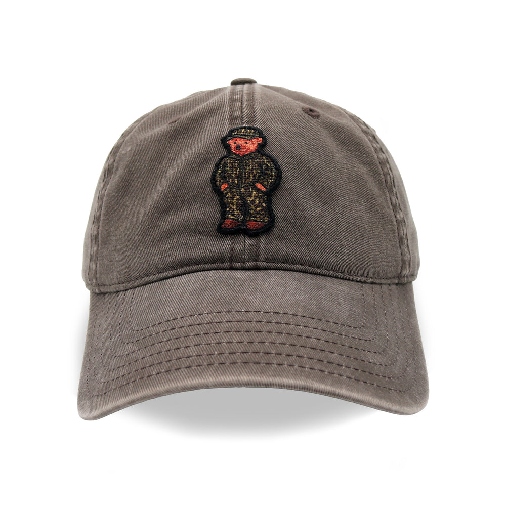 A washed gray cotton baseball cap featuring a central embroidered patch of a teddy bear in a camouflage uniform with red shoes and the word 'SPECIAL' on its hat.