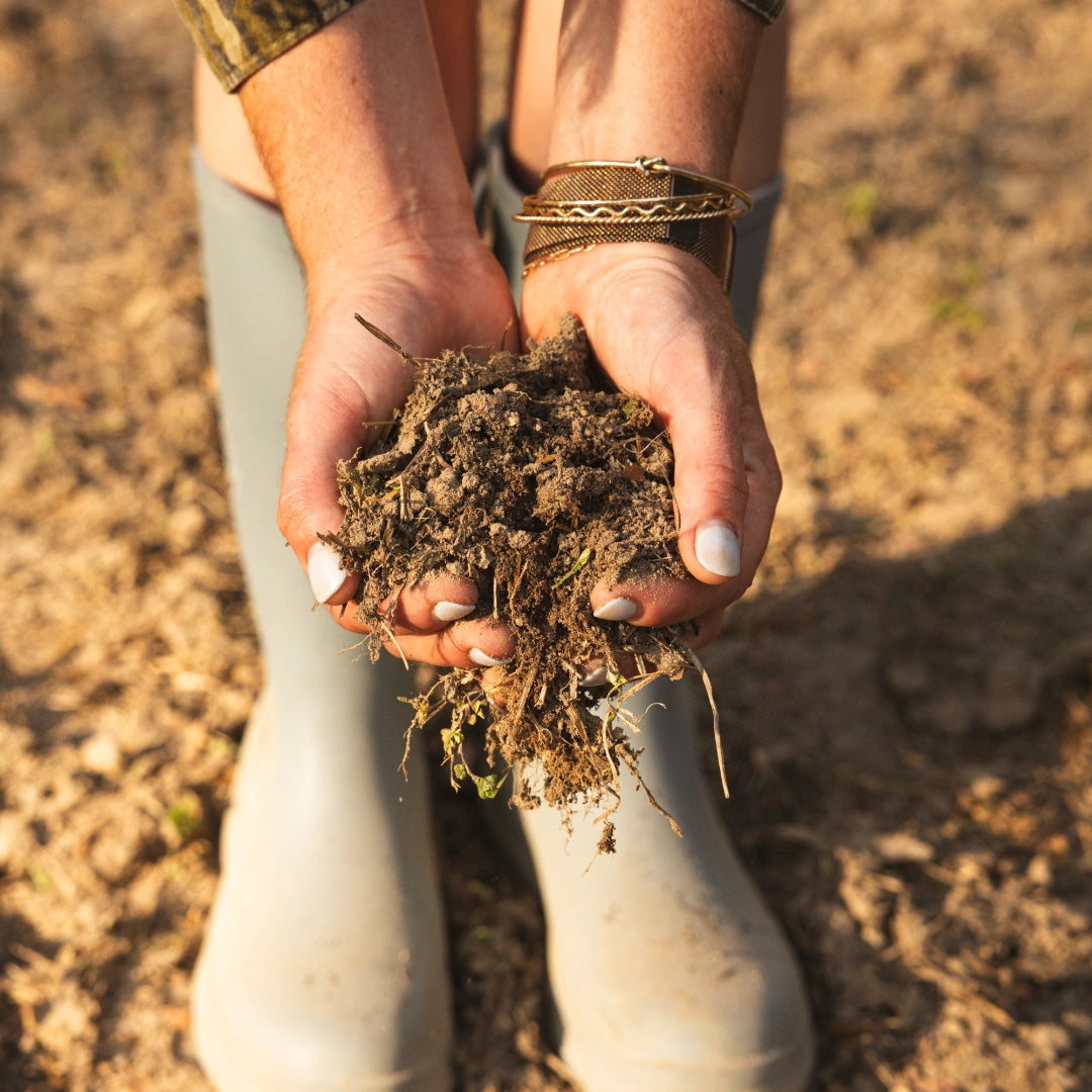 Macy holding a handful of soil with waders in the background